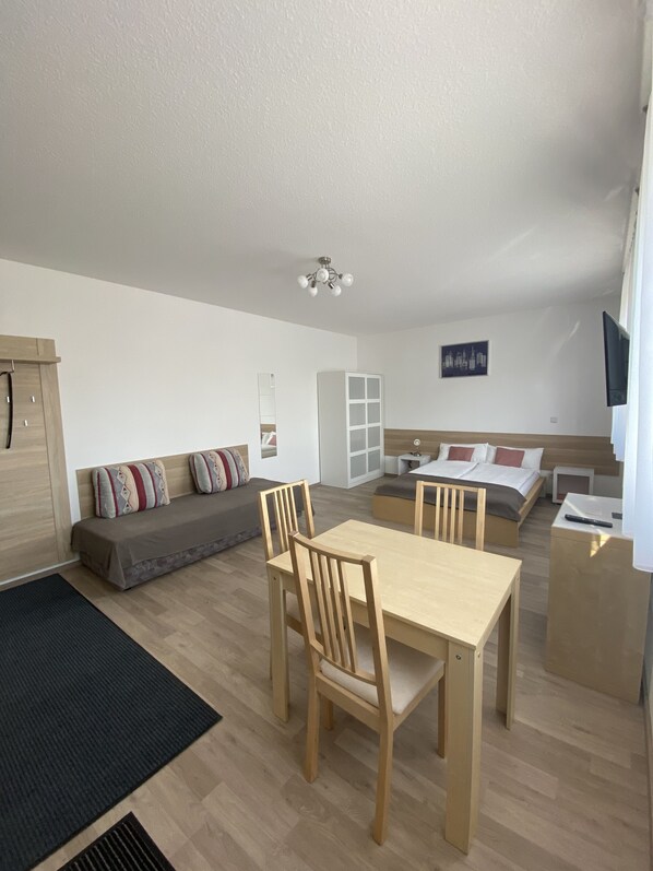 A modern, well-lit room with a dining table, chairs, a sofa, a bed, and a TV.
