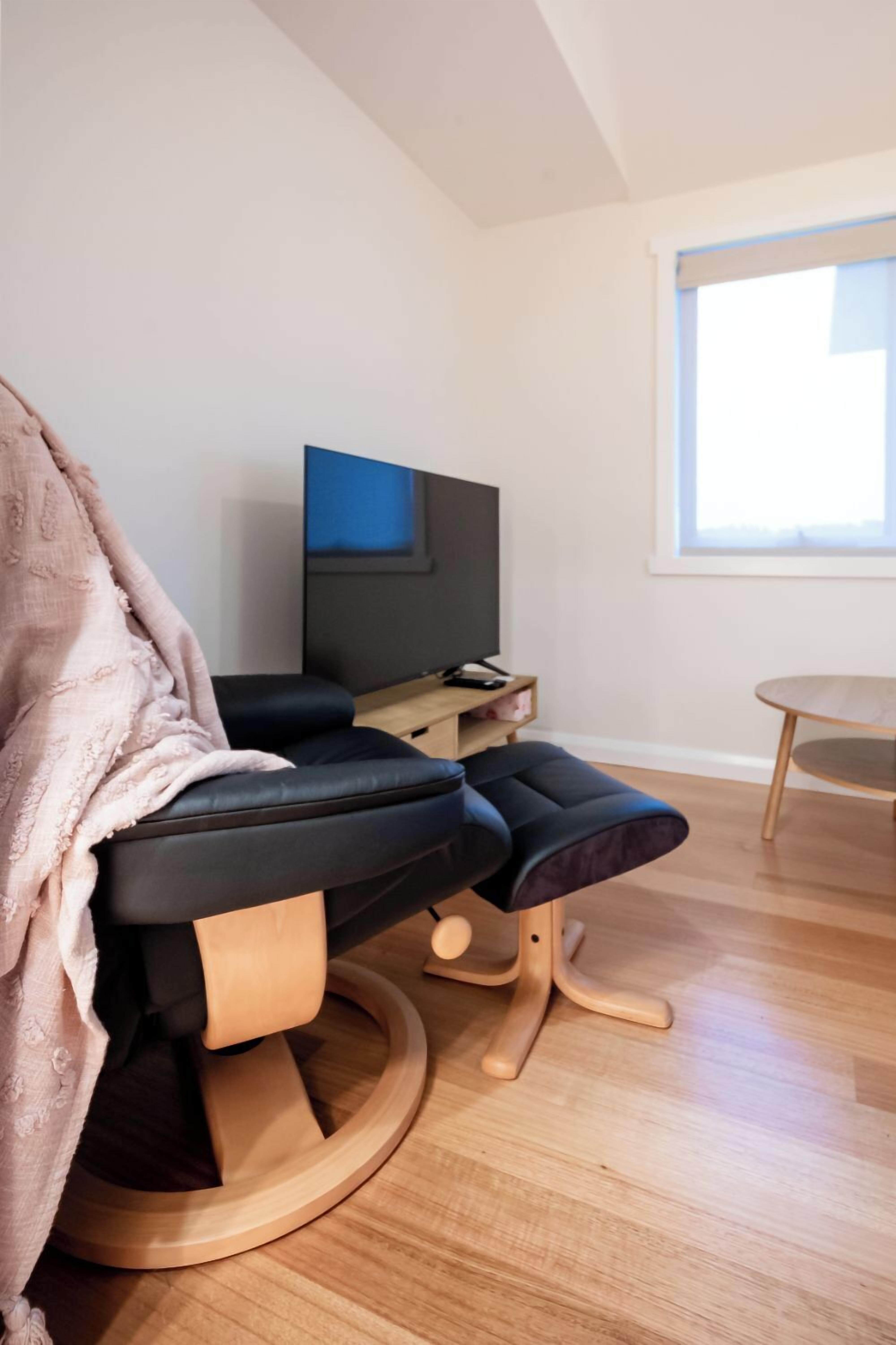 Een moderne woonkamer met een zwarte bank, een televisie en een houten vloer.