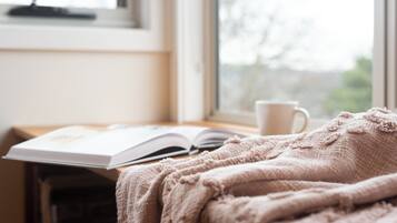 A cozy reading nook with a book, a cup, and a blanket by a window.