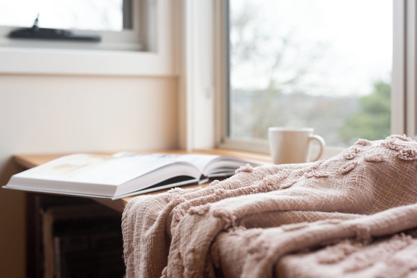 A cozy reading nook with a book, a cup, and a blanket by a window. - Modern Self Contained Unit Views, Parking and WiFi (South Launceston)