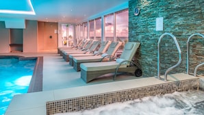 A hotel pool area with lounge chairs, a stone wall, and a view of the sunset.