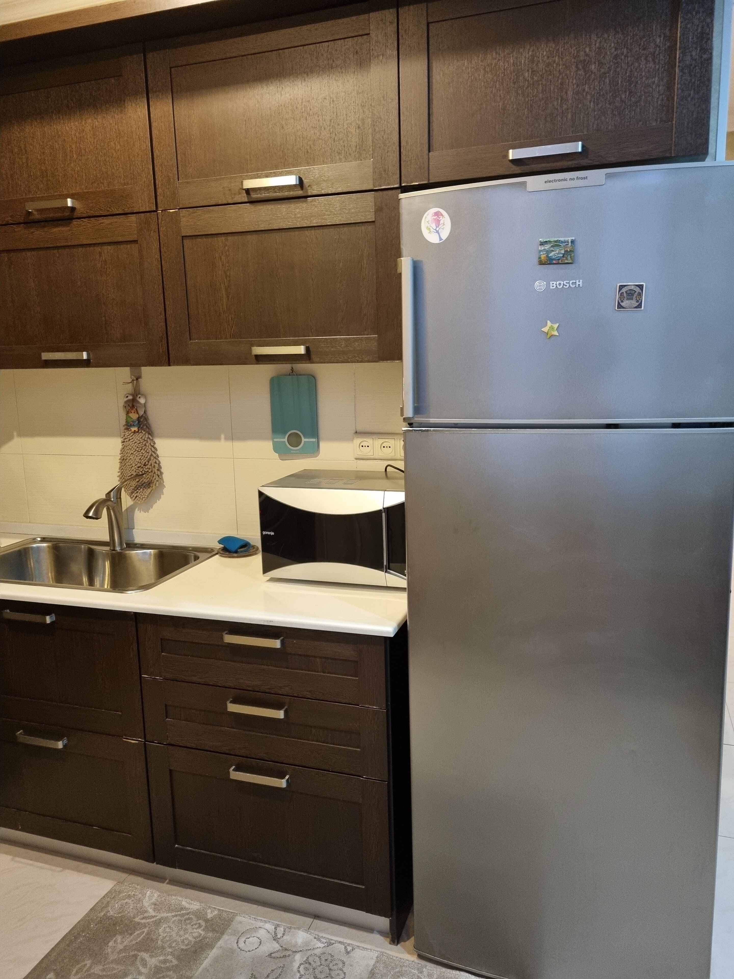 A kitchen with dark wooden cabinets, a stainless steel sink, and a Bosch refrigerator.
