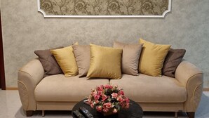 A living room with a beige sofa, multiple cushions, a black coffee table with a floral arrangement, and a patterned wall hanging. - Niniko's Old Tbilisi Historical House. (Tbilisi)