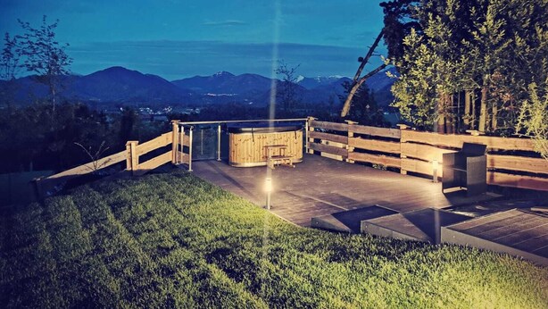 A wooden deck with a hot tub, surrounded by a wooden fence, overlooking a mountainous landscape.