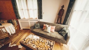 A cozy living room with a grey sofa, a glass coffee table with wood logs, a wooden dining table, and a cowhide rug.
