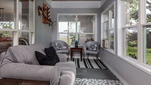 Una sala de estar acogedora con un sofá gris, dos sillones, una mesa de centro y vistas al exterior a través de grandes ventanales.