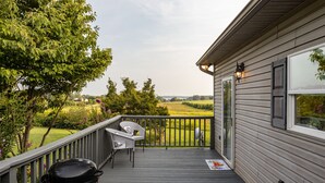 Una terraza con una parrilla, mobiliario exterior y vistas a un paisaje verde.