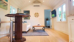 Une pièce spacieuse dotée d’un plancher en bois, d’une table centrale avec un piétement en bois foncé, d’un canapé blanc et d’un tapis à rayures.