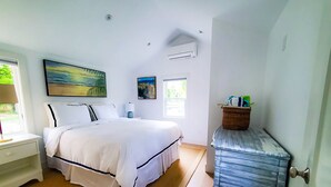 Une chambre à coucher comprenant un lit, une table de chevet, une lampe, un tableau, un appareil de climatisation et une fenêtre.