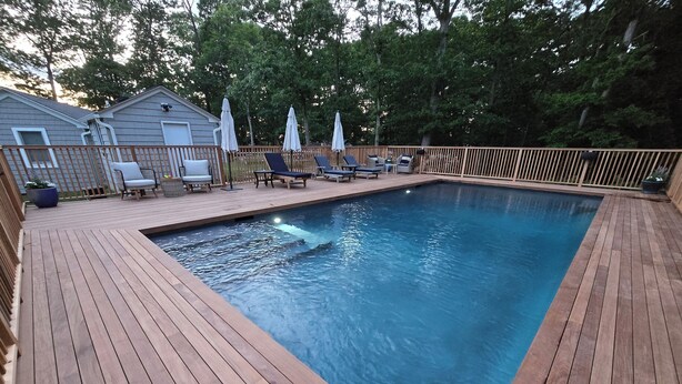 Une terrasse en bois avec une piscine, des chaises longues et des parasols.