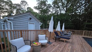 Une terrasse en bois avec des chaises longues et des parasols, une petite table ornée d’objets colorés, et une piscine en arrière-plan.