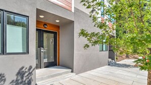 A modern building with a glass door entrance, a number '106' sign above the door, and a paved patio area.