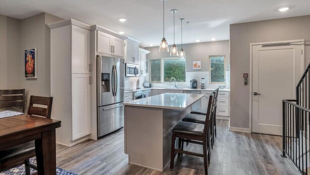 A modern kitchen with stainless steel appliances, a central island, pendant lighting, and a view of the outdoors.