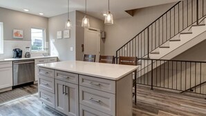 A kitchen with a central island, stainless steel appliances, pendant lighting, and a staircase with a railing.