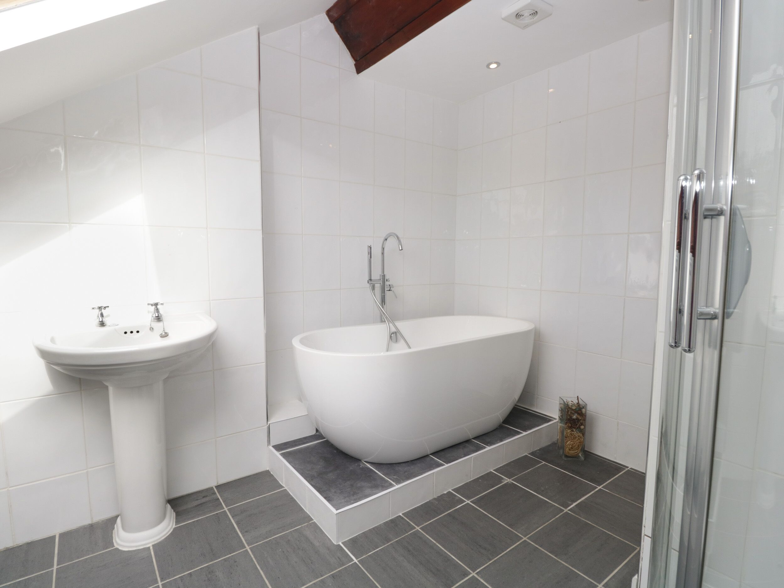 A modern bathroom with a freestanding bathtub, a pedestal sink, and a glass shower enclosure.
