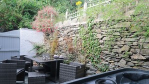 Un espace avec un jacuzzi, agrémenté de meubles en osier et d’un mur en pierre.