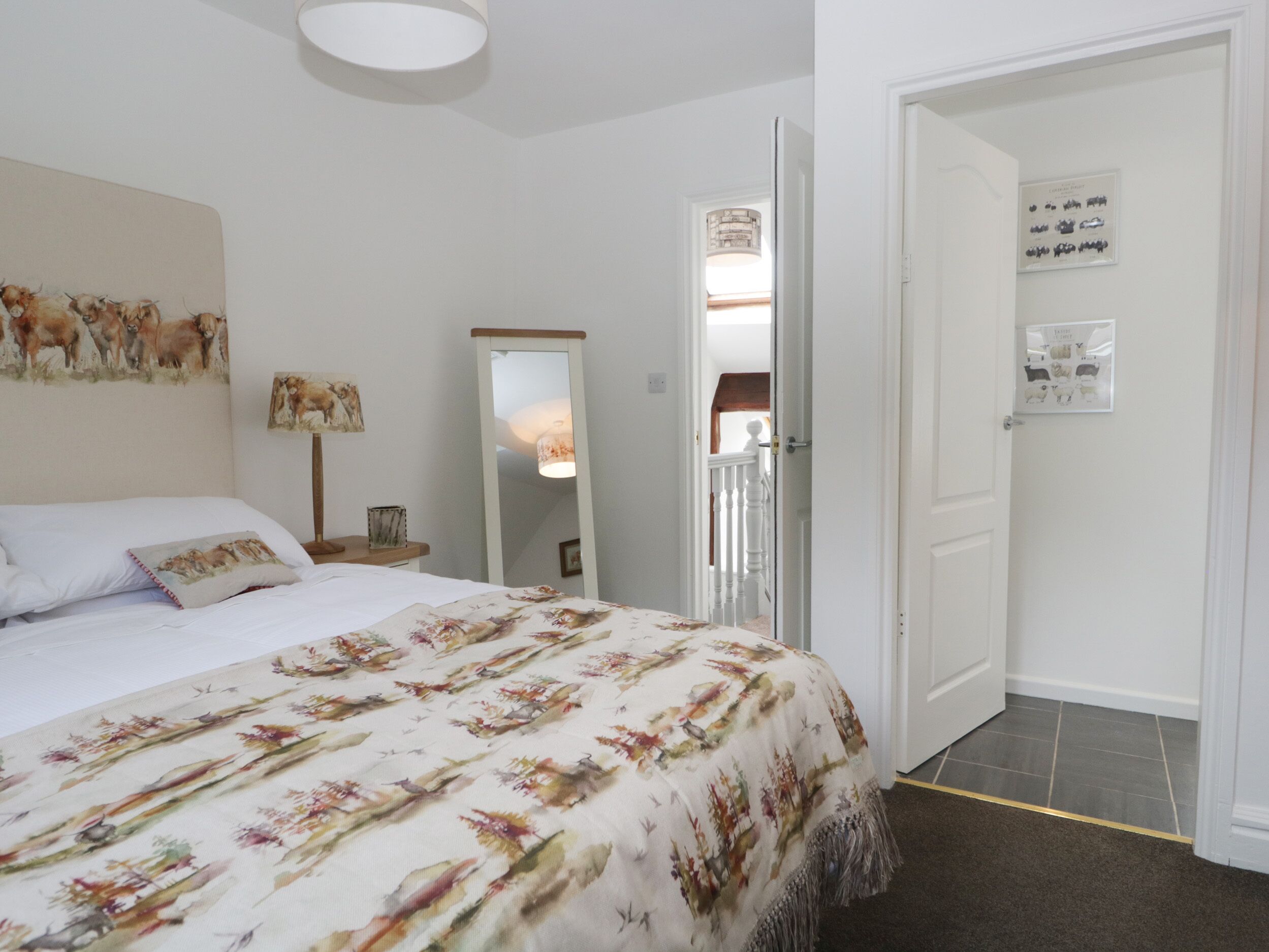 A bedroom with a bed, a mirror, a painting of animals, and a door leading to another room.