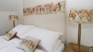 Une chambre à coucher avec un grand tableau représentant du bétail accroché au mur, du linge de lit blanc et deux lampes de chevet.