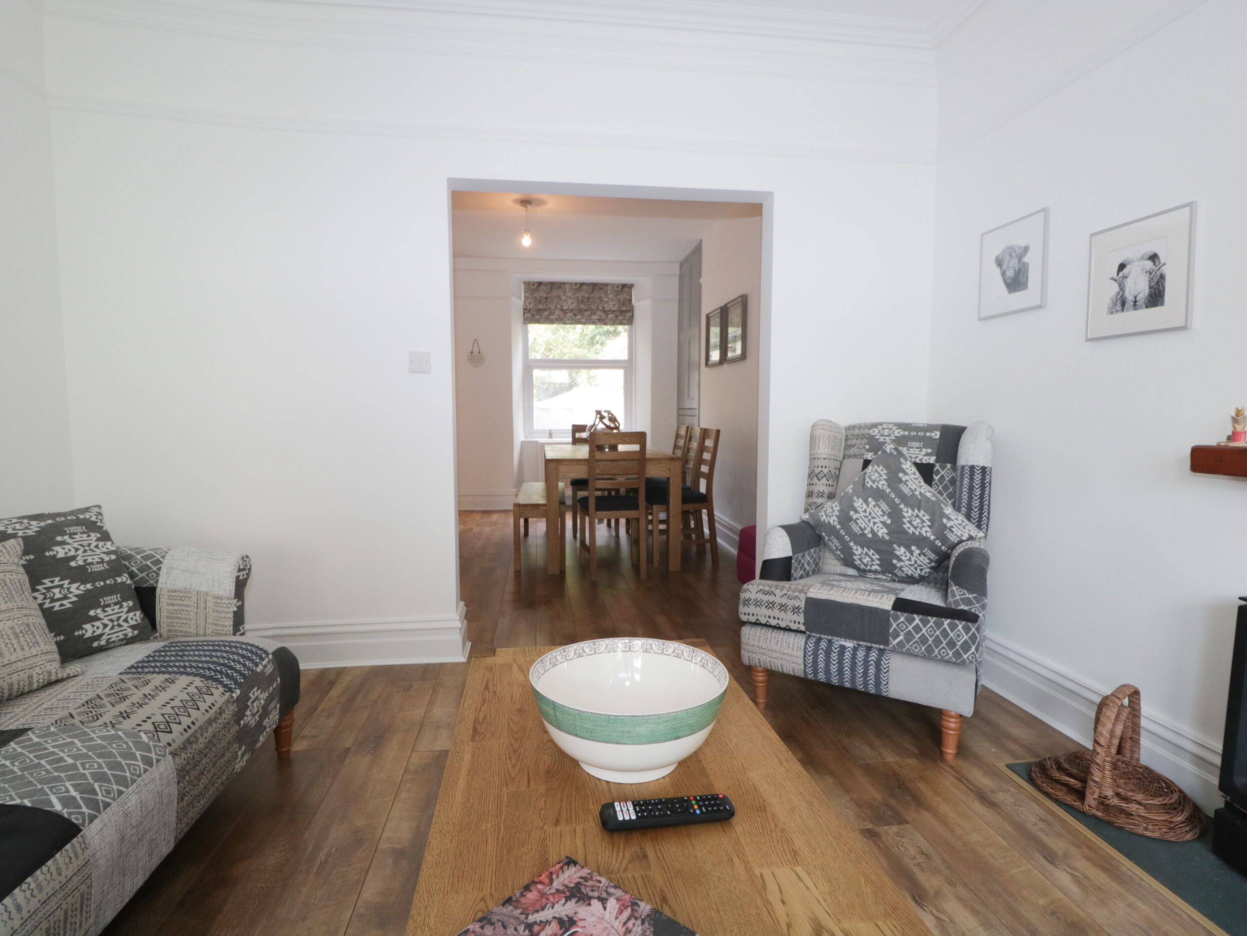 A living room with a sofa, a patterned armchair, a dining area with a table and chairs, and a large bowl on the floor.
