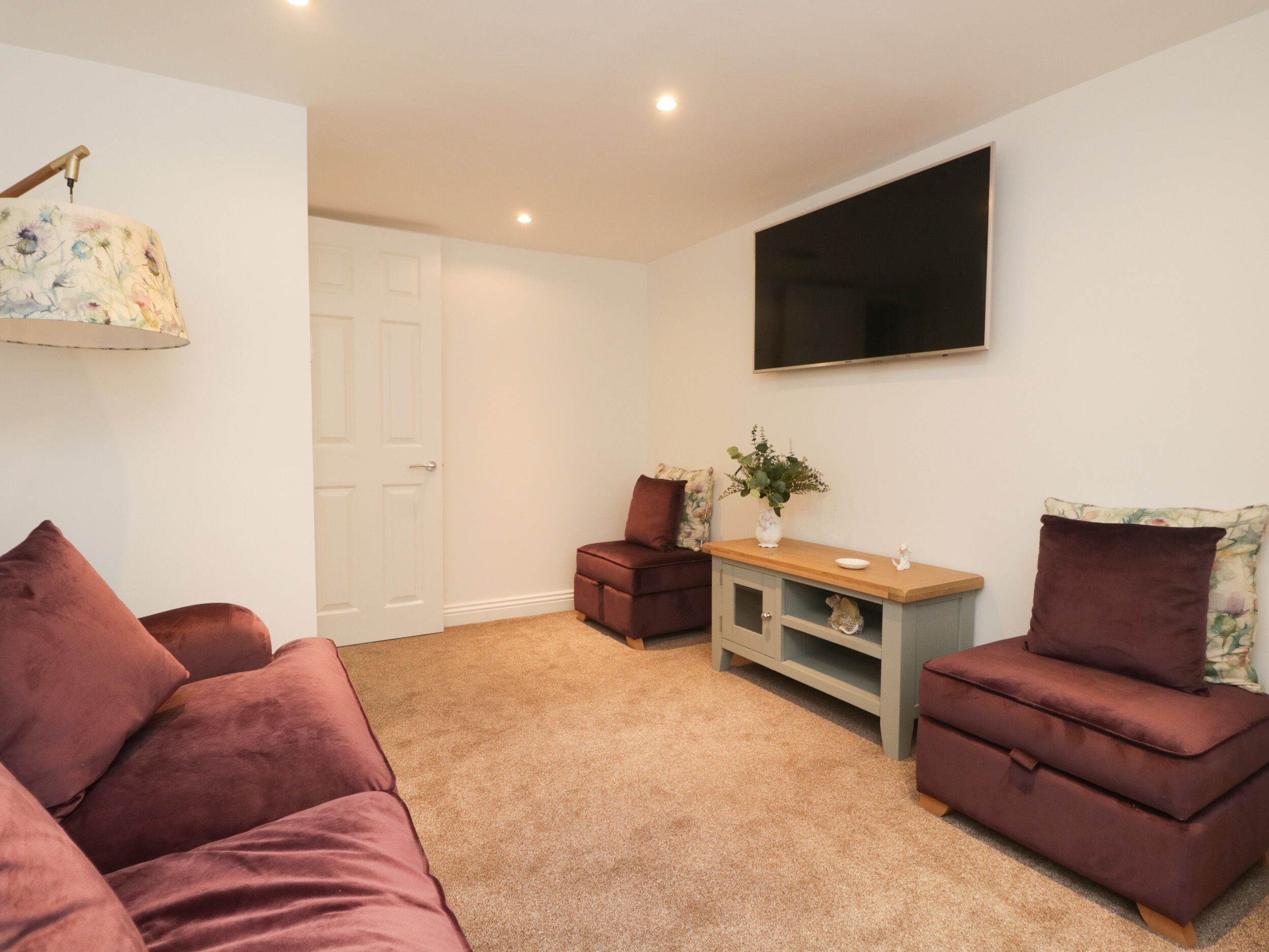 A living room with a sofa, a chair, a small table with a plant, and a flat-screen TV mounted on the wall.