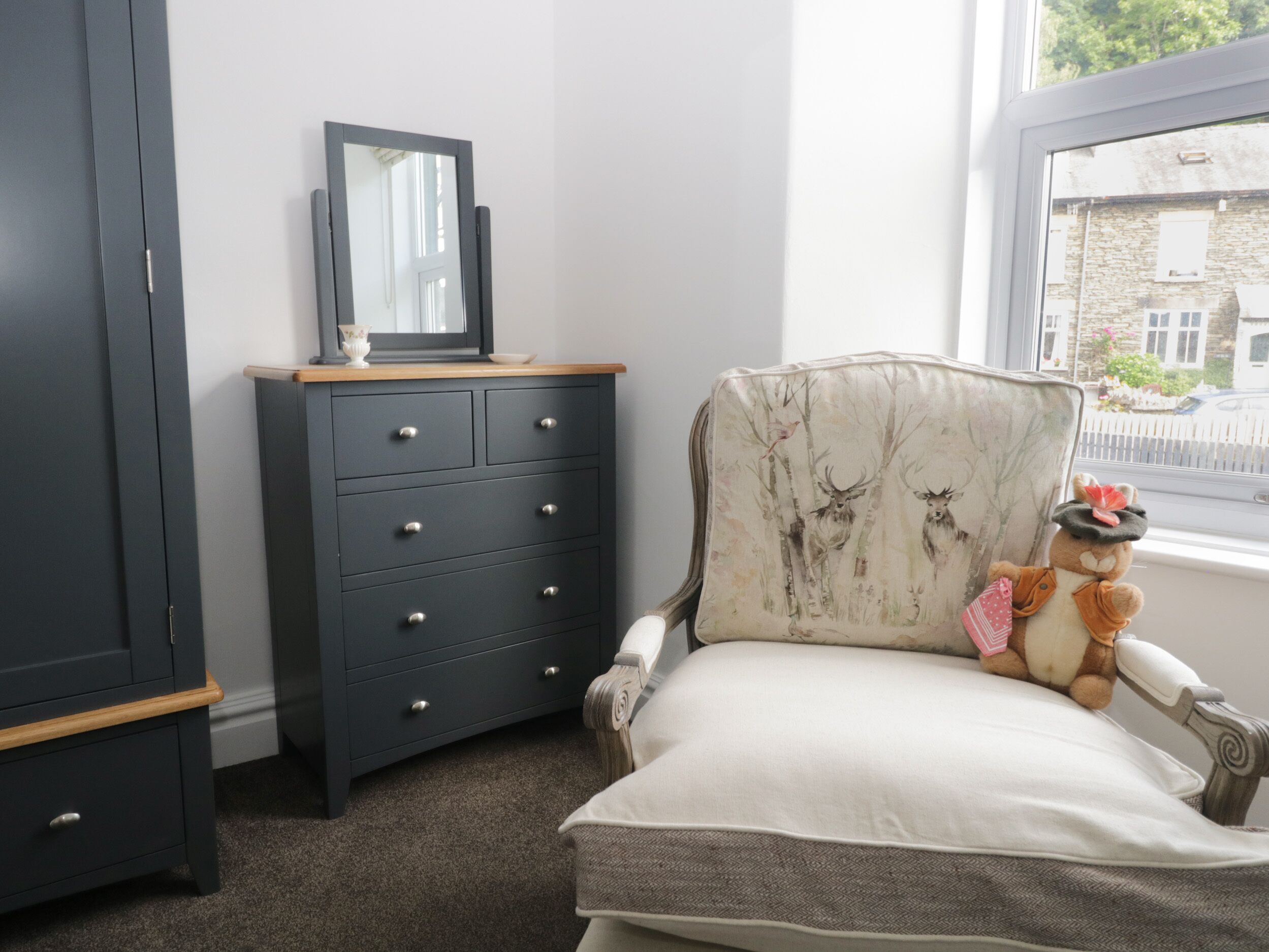 A bedroom with a bed, a dresser, a mirror, and a window with a view of buildings.