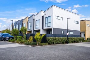 A modern apartment building with a row of townhouses, a parking area, and a blue car parked in front. - Huntington Townhouse with Patio and Parking (Auckland East)