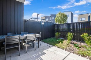 A patio with a table and chairs, a wooden fence, and a small garden area. - Huntington Townhouse with Patio and Parking (Auckland East)