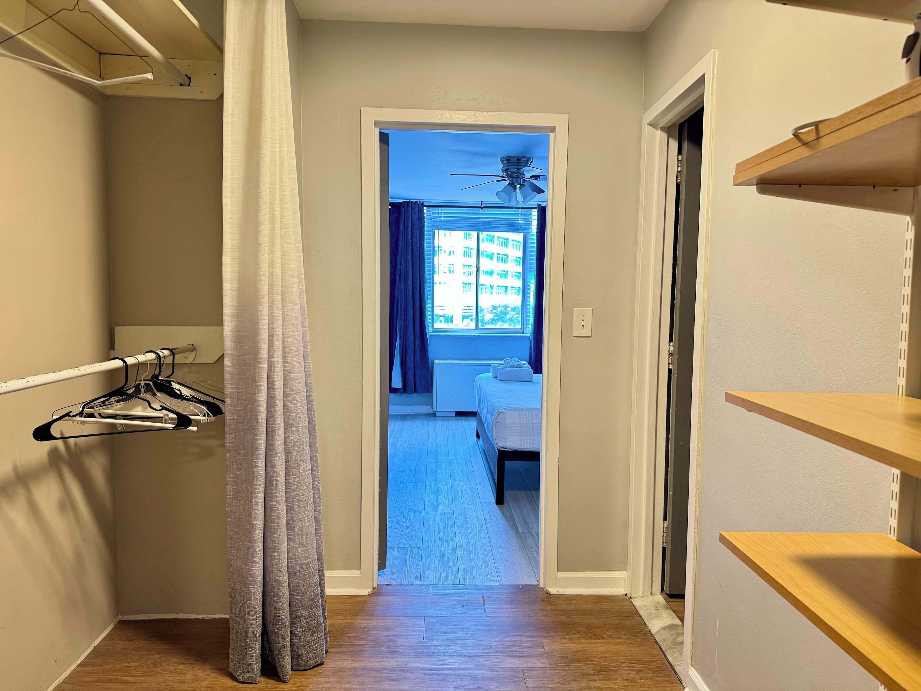 Un couloir avec un lit, un ventilateur de plafond et une fenêtre avec des rideaux.
