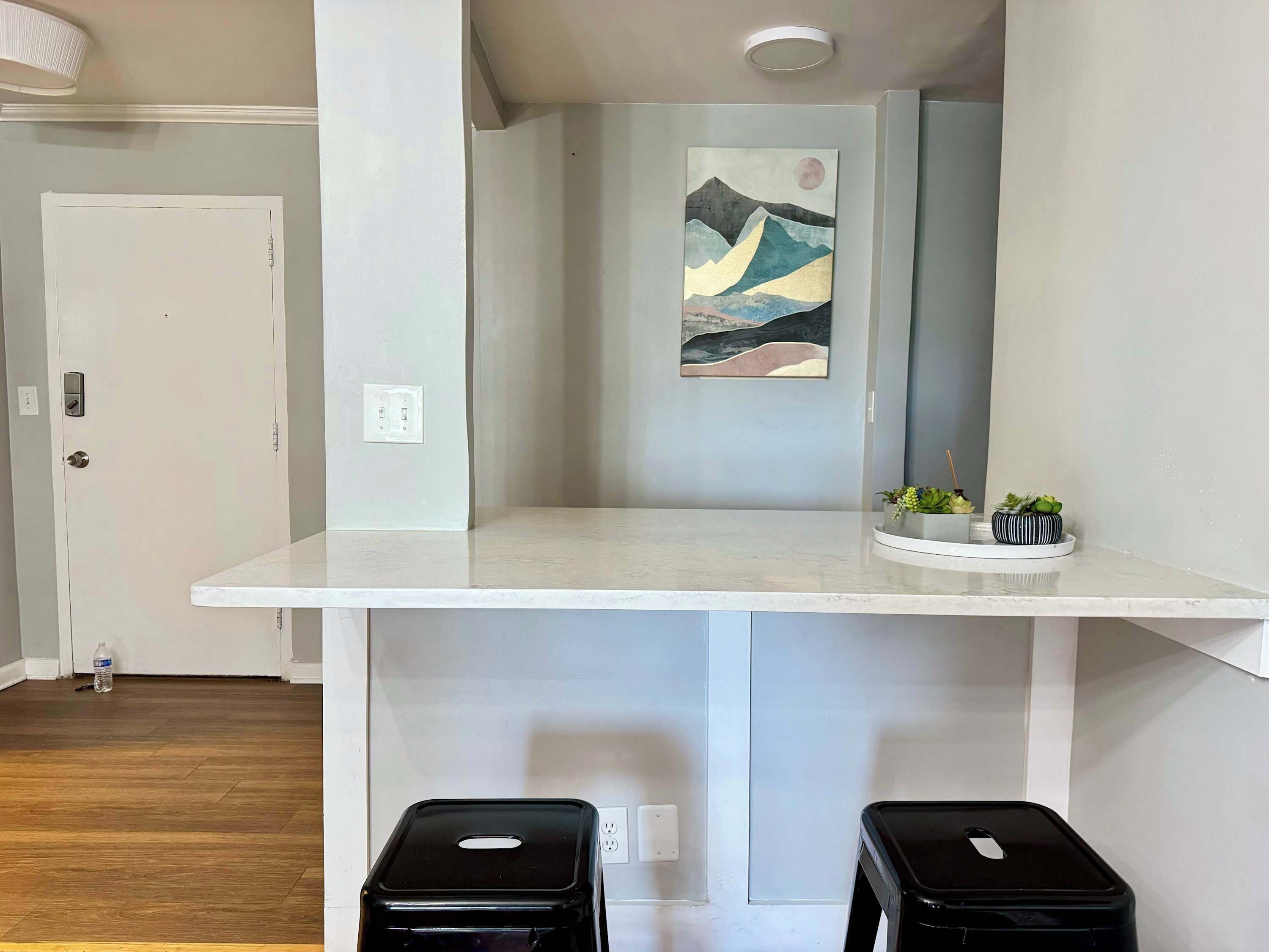 A modern bathroom with a white vanity, a painting on the wall, and a small plant on the counter.