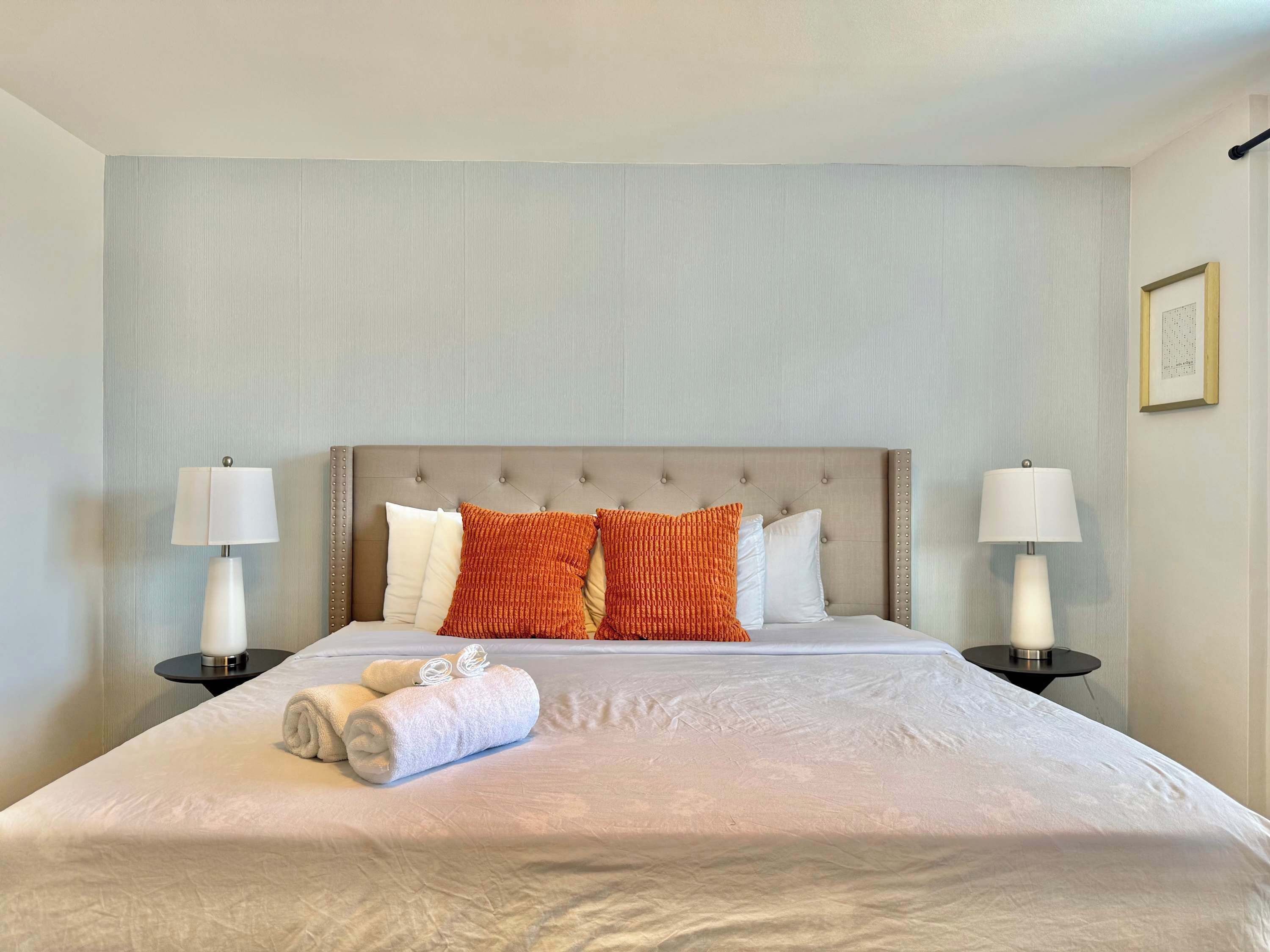 A neatly made bed with a headboard, two bedside tables with lamps, and a framed picture on the wall.