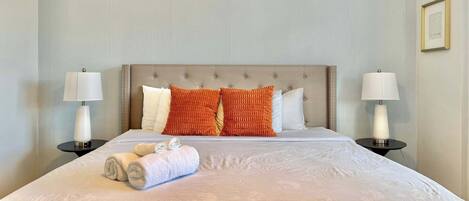 A neatly made bed with a headboard, two bedside tables with lamps, and a framed picture on the wall.