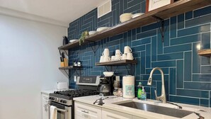 A modern kitchen with a gas stove, oven, white cabinets, a stainless steel sink, and blue patterned backsplash.