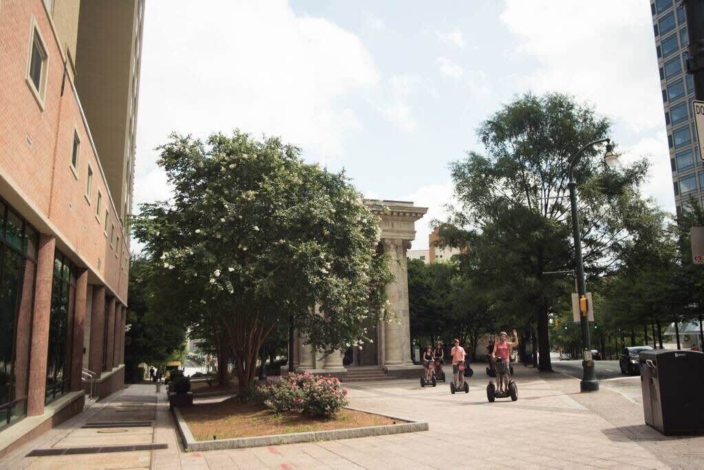 Pátio com árvores, uma fonte e pessoas andando em Segways.