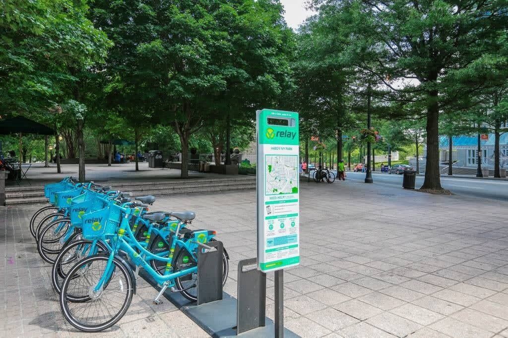 Un espacio público con una estación de bicicletas compartidas y un cartel con un mapa.