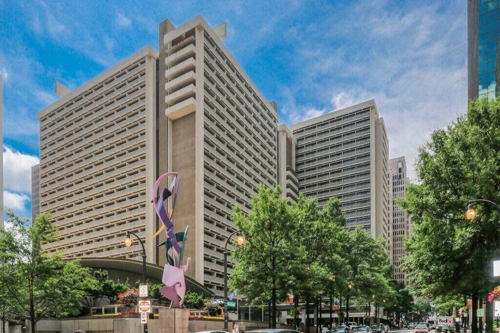 Une rue moderne en milieu urbain, bordée d’immeubles imposants, avec un trottoir piétonnier et une grande sculpture abstraite.