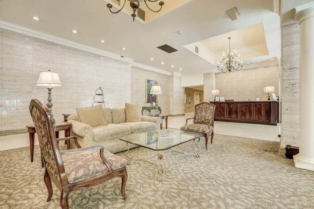A spacious lobby with a sofa, chairs, a glass coffee table, a reception desk, and a chandelier.