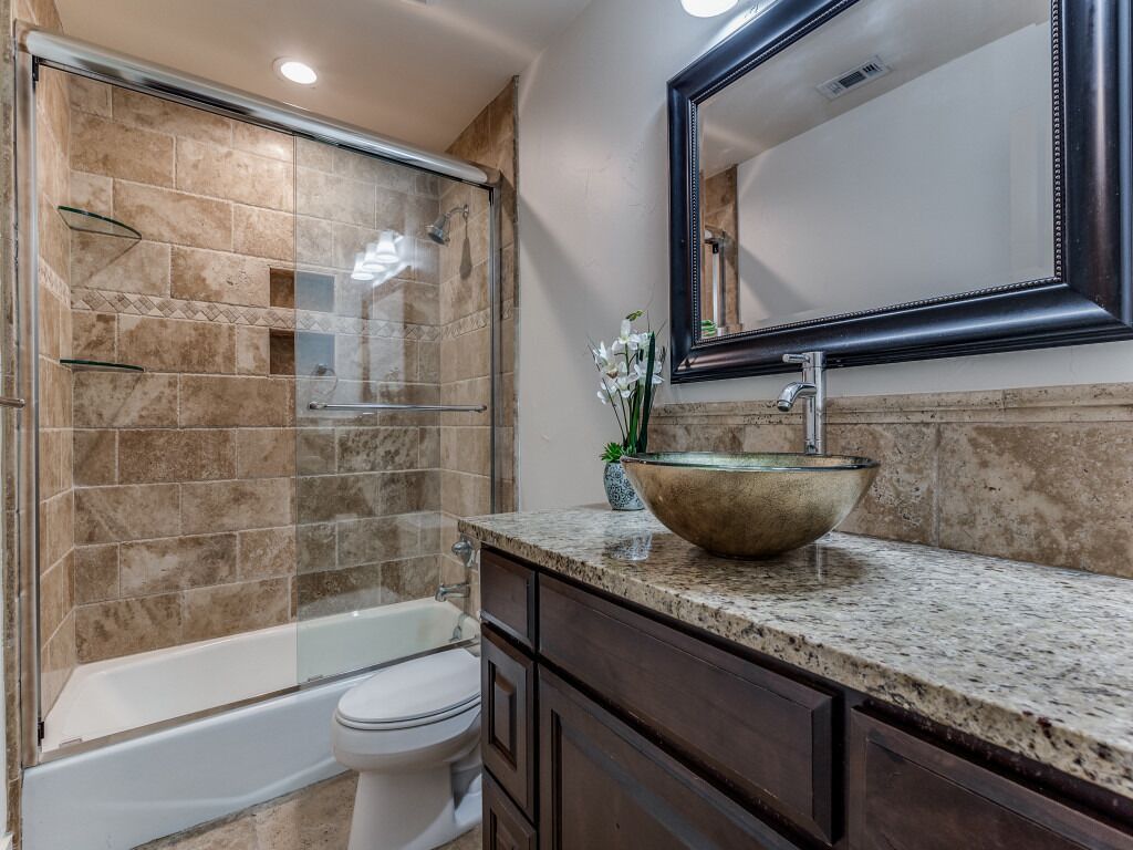 A bathroom with a glass-enclosed shower, a white toilet, a large vessel sink, and dark wooden cabinets.