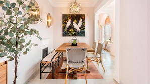 A dining area with a wooden table, black and white wicker chairs, a wall-mounted painting of birds, and a hanging star-shaped light fixture. - Genteel Home San Isidoro Terrace (Seville)