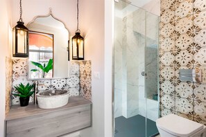 Une salle de bain avec un lavabo en marbre, deux lanternes suspendues, une plante en pot et une douche aux carreaux décorés.
