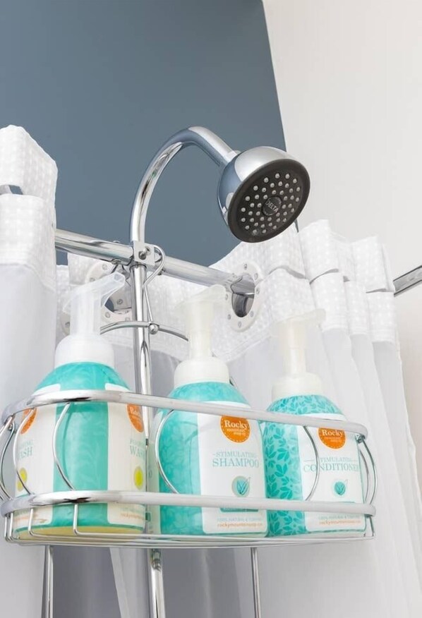 A bathroom with a shower head, a metal rack holding bottles of shampoo and conditioner, and a towel rack.