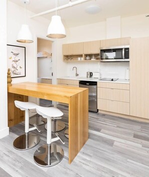 A modern kitchen with a wooden island, white bar stools, a stainless steel sink, and a microwave.