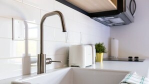 A modern kitchen with a stainless steel faucet, white tiles, a toaster, and a small potted plant. - Sparkling Clean, Cozy and Comfortable in Highlands (Edmonton)