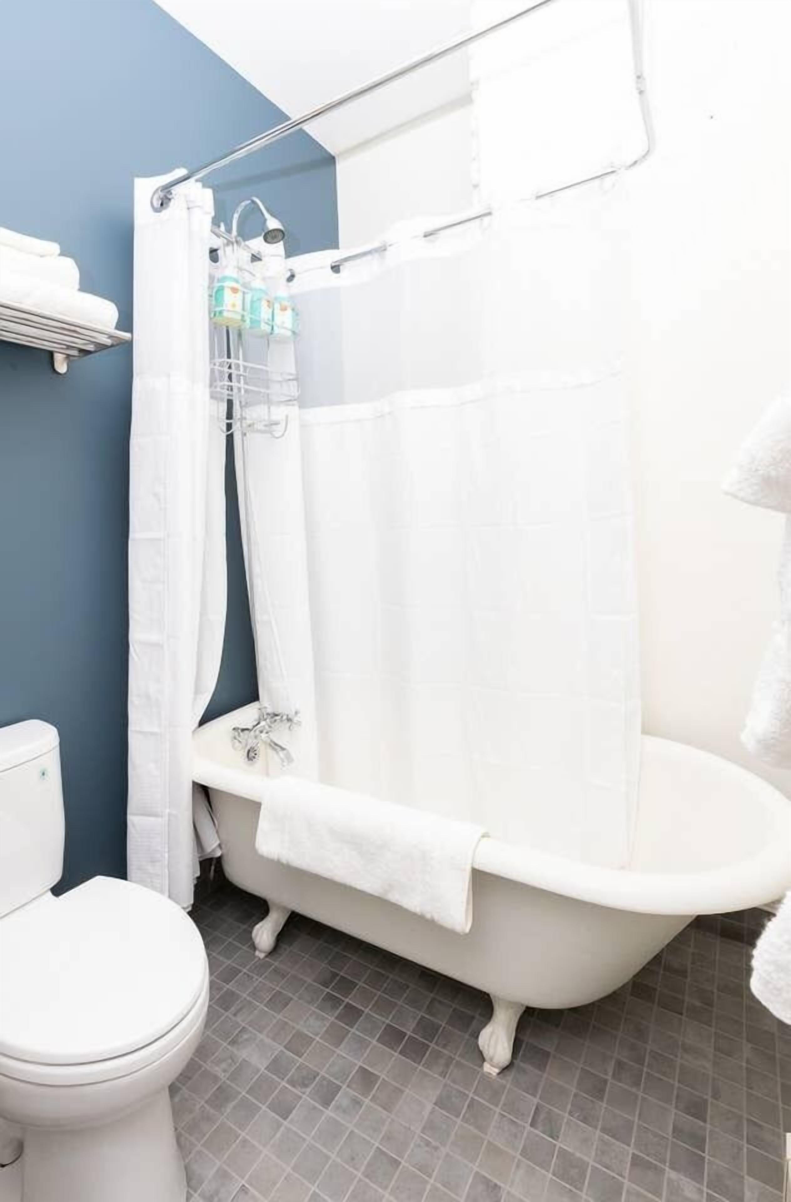A bathroom with a white bathtub, a shower curtain, a toilet, and a towel rack.