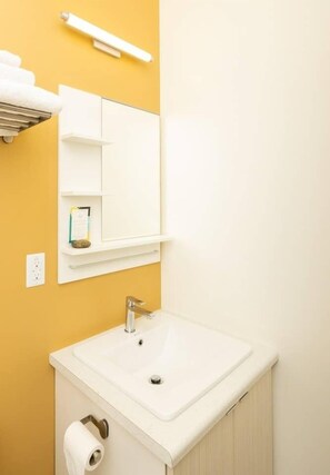 Een badkamer met een wit wastafel, spiegel, handdoekhouder en toiletrolhouder.