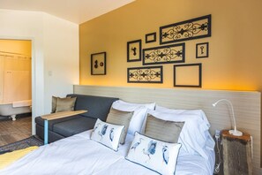 A hotel room with a bed, a sofa, a bedside table, and a wall with framed artwork. - Clean Sophisticated Comfort in Highlands (Edmonton)