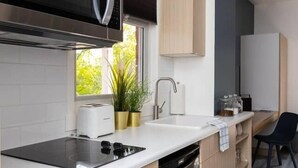 A modern kitchen with a built-in microwave, stove, and sink. There is a window with a view of greenery outside. - Clean, Charming & Cozy Sanctuary in Highlands (Edmonton)
