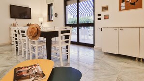 A dining area with white chairs, a table with a magazine, and a view through a glass door to the outside. - Villa (Torre Vado)