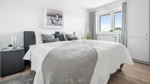 Una camera da letto moderna con un letto grande, un comodino con una lampada, un quadro appeso al muro e una finestra con tende.