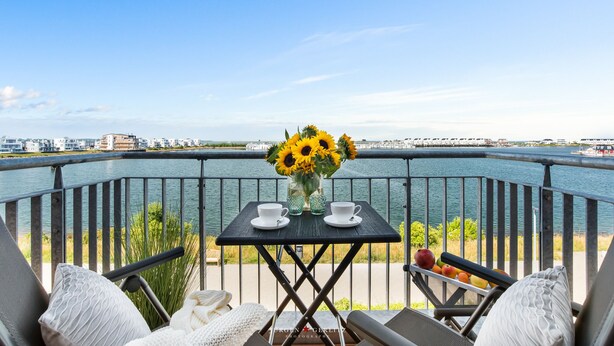 Un balcone con un tavolo apparecchiato per due, affacciato su uno specchio d'acqua e una costa lontana.