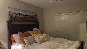 A bedroom with a bed, a headboard, a painting above the bed, and a window with blinds. - Quit friendly Neighborhood  (Anthem)